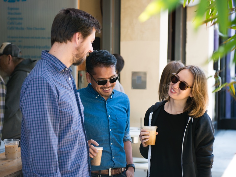 Three people standing together outside with coffees in their hands.